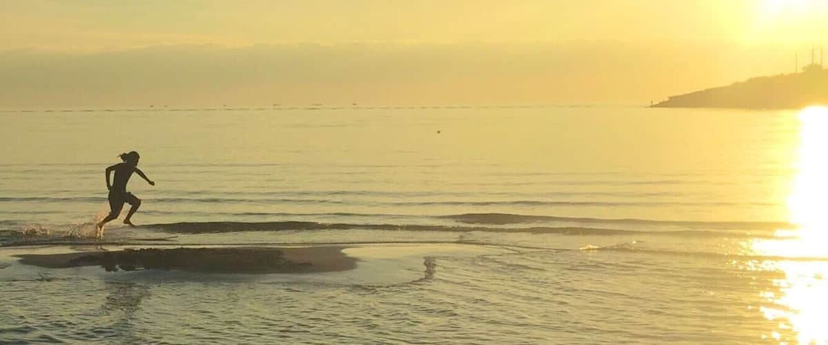 A person running along a beach at sunset with the sun low on the horizon.