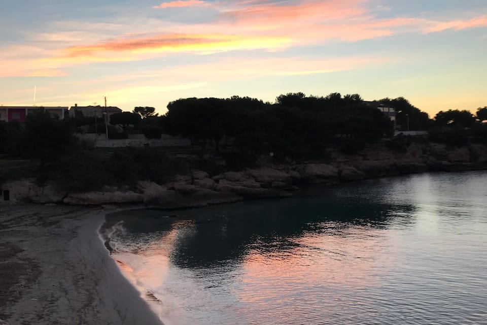 A sunset over a river with a beach and trees in the background.