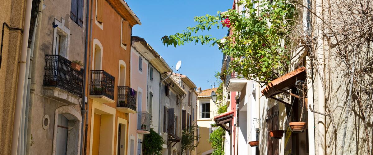 A narrow street with old buildings, a clear blue sky, and a tree with green leaves.