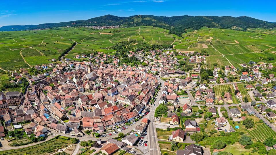 A village with red-roofed houses surrounded by green fields and mountains in the background.