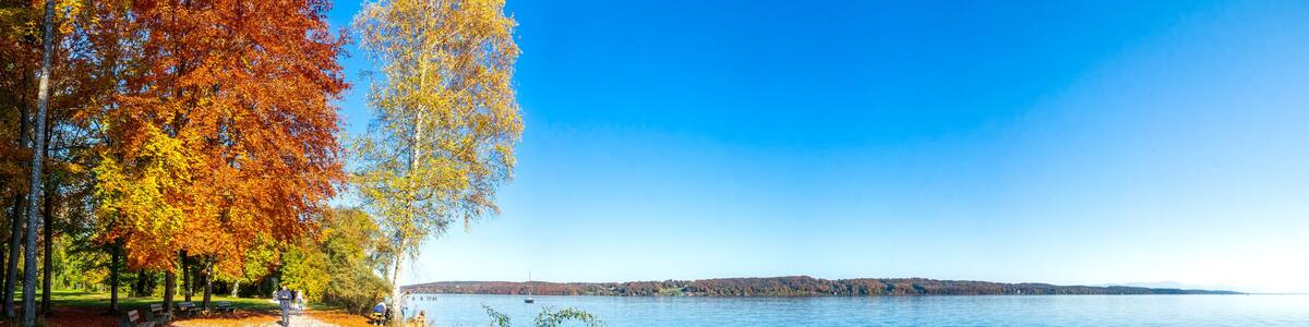 Ein See mit Herbstlaub, einem klaren Himmel und einer fernen Uferlinie.