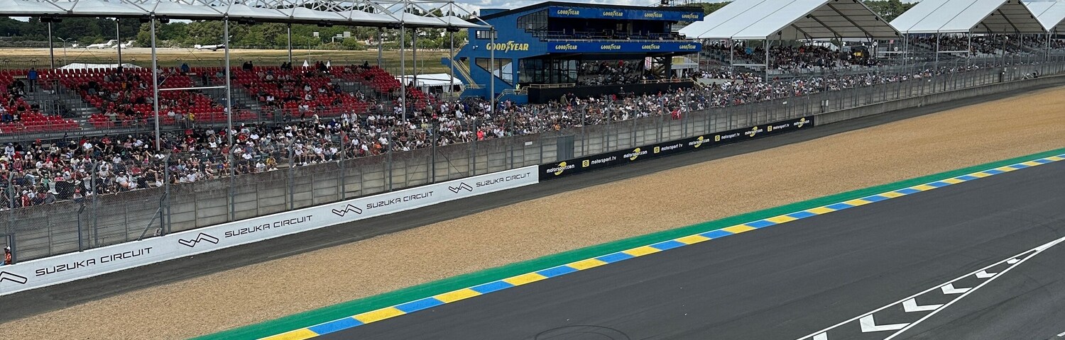 A race track with grandstands, a clear sky, and a Rolex logo.