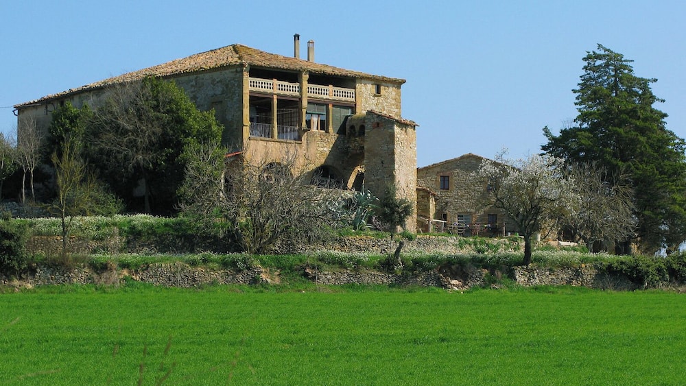 Ein Steinhaus mit Balkon, umgeben von Grün und einer Steinmauer.