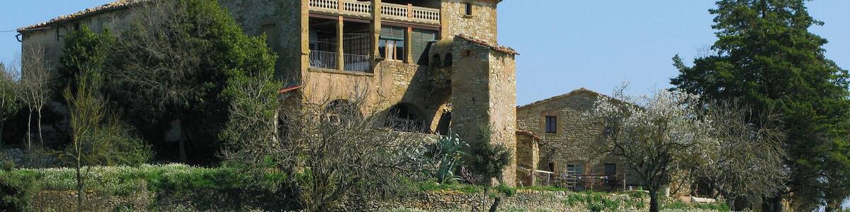 Une maison en pierre dotée d’un balcon, entourée de verdure et d’un mur en pierre.
