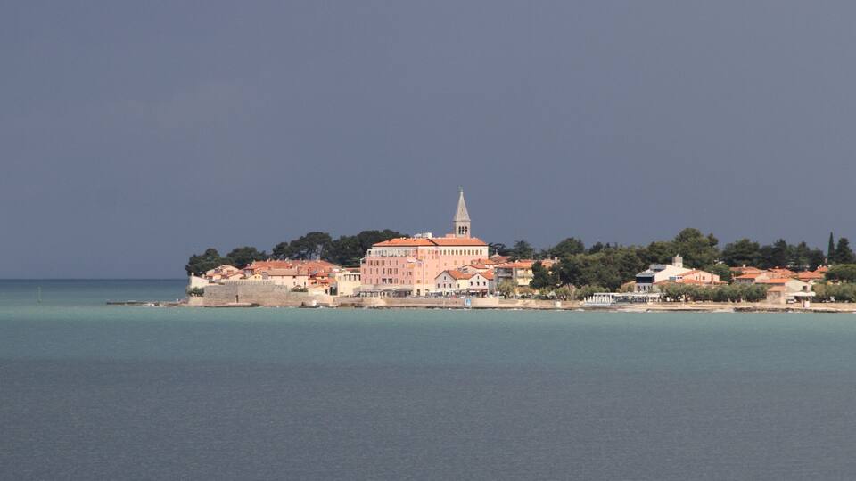 A coastal town with a prominent church and a tower, surrounded by clear waters and greenery.