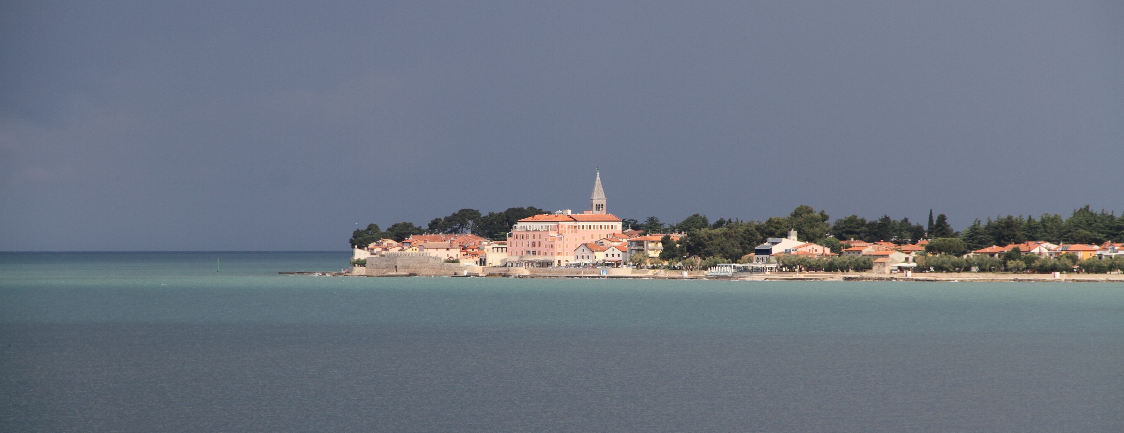 A coastal town with a prominent church and a tower, surrounded by clear waters and greenery.