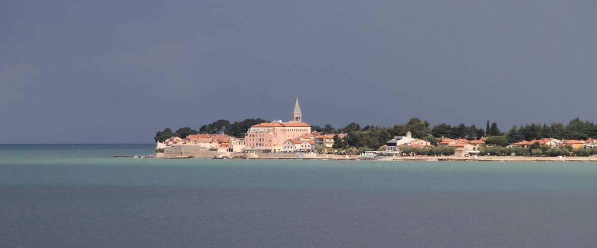A coastal town with a prominent church and a tower, surrounded by clear waters and greenery.