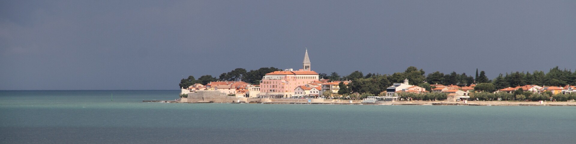 A coastal town with a prominent church and a tower, surrounded by clear waters and greenery.