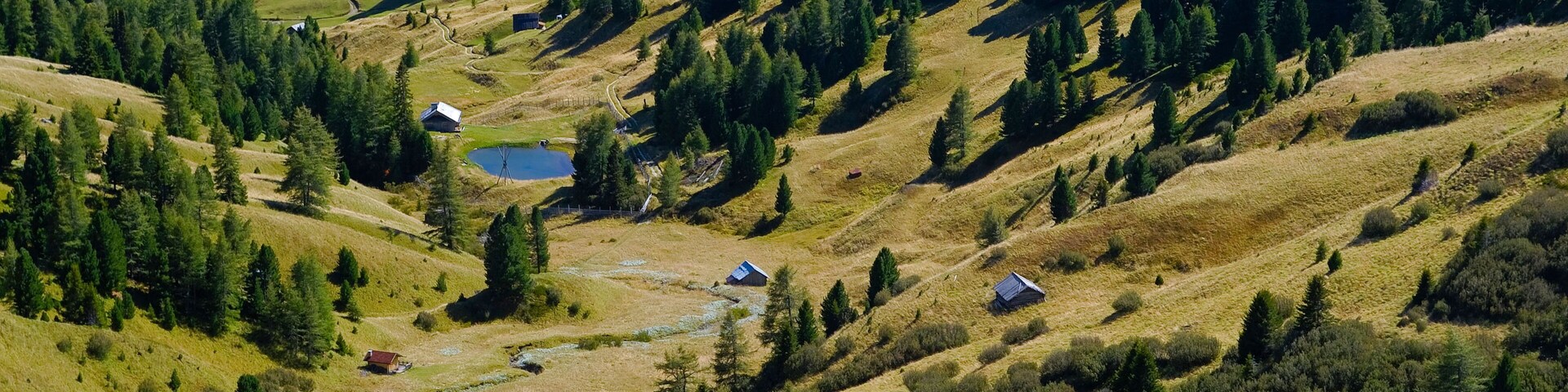 Paisagem montanhosa com casas dispersas, um rio e florestas densas.