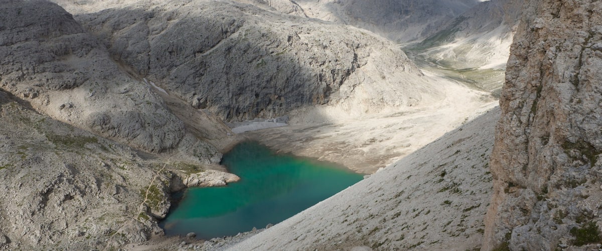 Un paysage montagneux avec un lac turquoise, entouré de terrains rocheux et dominé par d’imposants sommets.