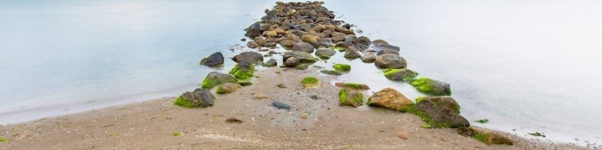 A rocky pier extending into calm waters with a clear sky.