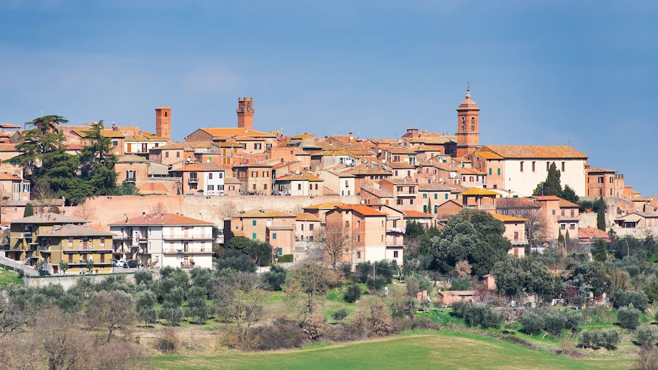 A historic town with terracotta-roofed buildings, prominent towers, and lush greenery.
