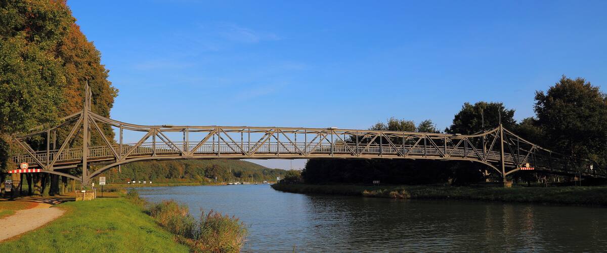 A steel bridge over a river with a path beside it.