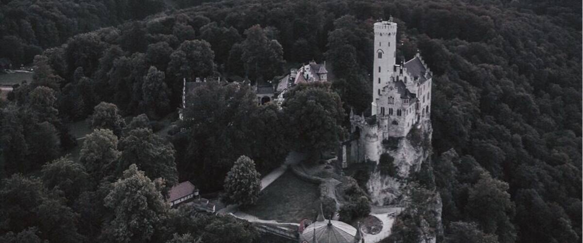 A castle surrounded by dense forest with a sunset in the background.