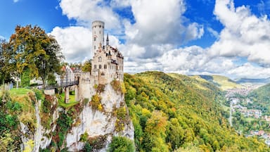 Um castelo empoleirado em um penhasco, com vista para um vale e uma cidade lá embaixo.