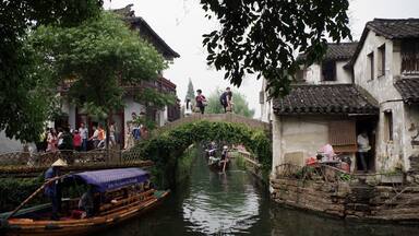 A narrow waterway with traditional boats, a stone bridge, and old buildings.