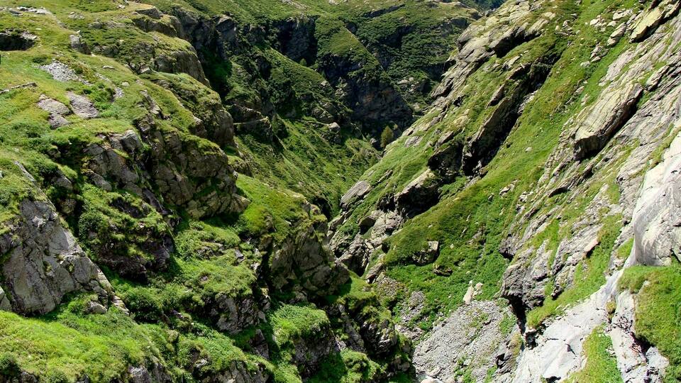 A mountainous landscape with a narrow valley, rocky terrain, and lush green vegetation.