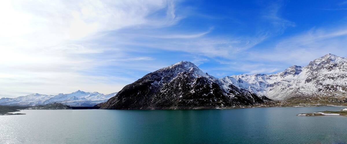 A snow-capped mountain range with a lake in the foreground.