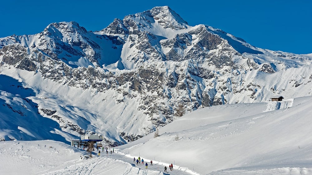 Une montagne enneigée, avec une station de ski et un petit chalet.