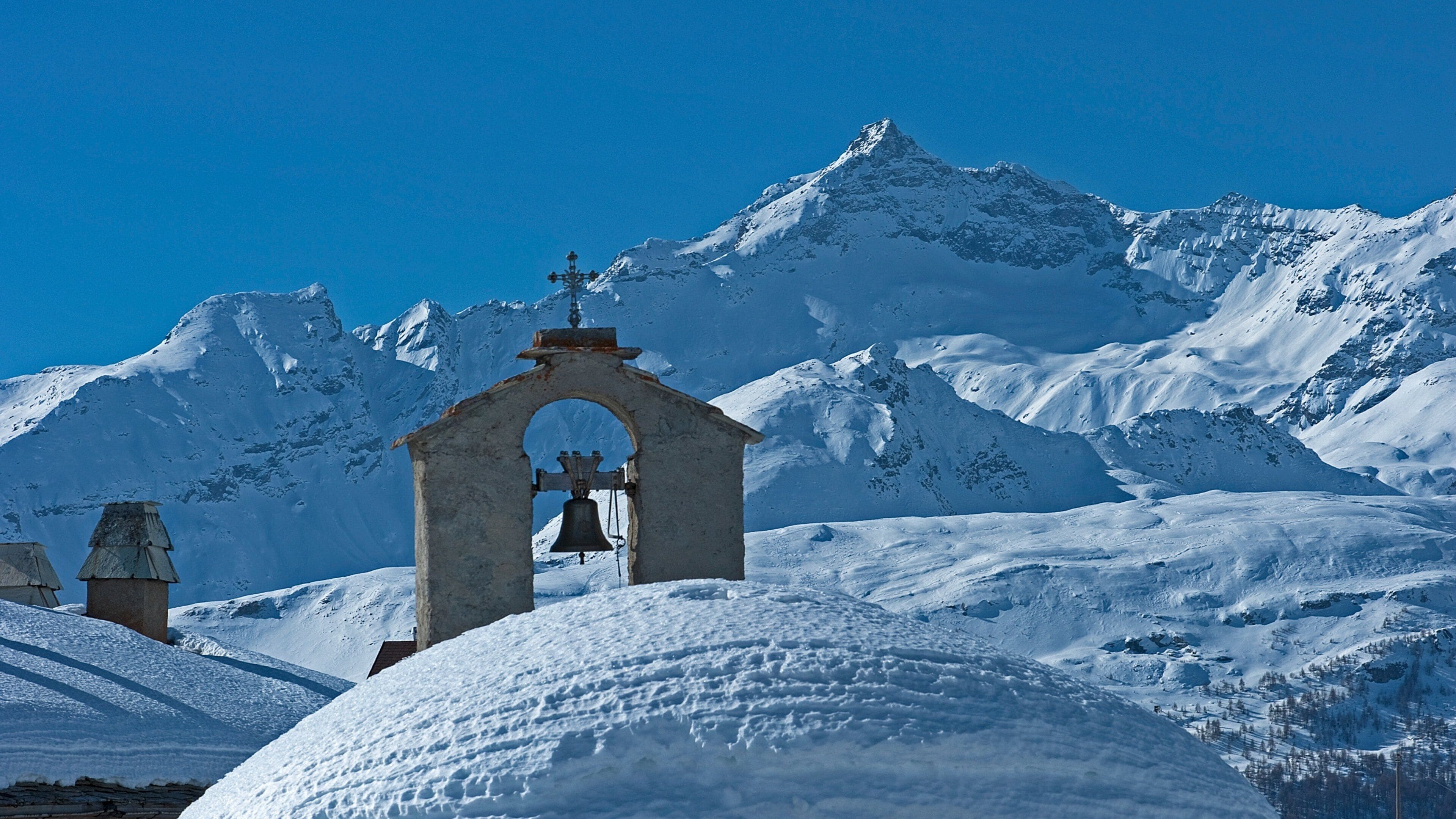 A snow-covered mountain range with a church bell tower and a cross on top.