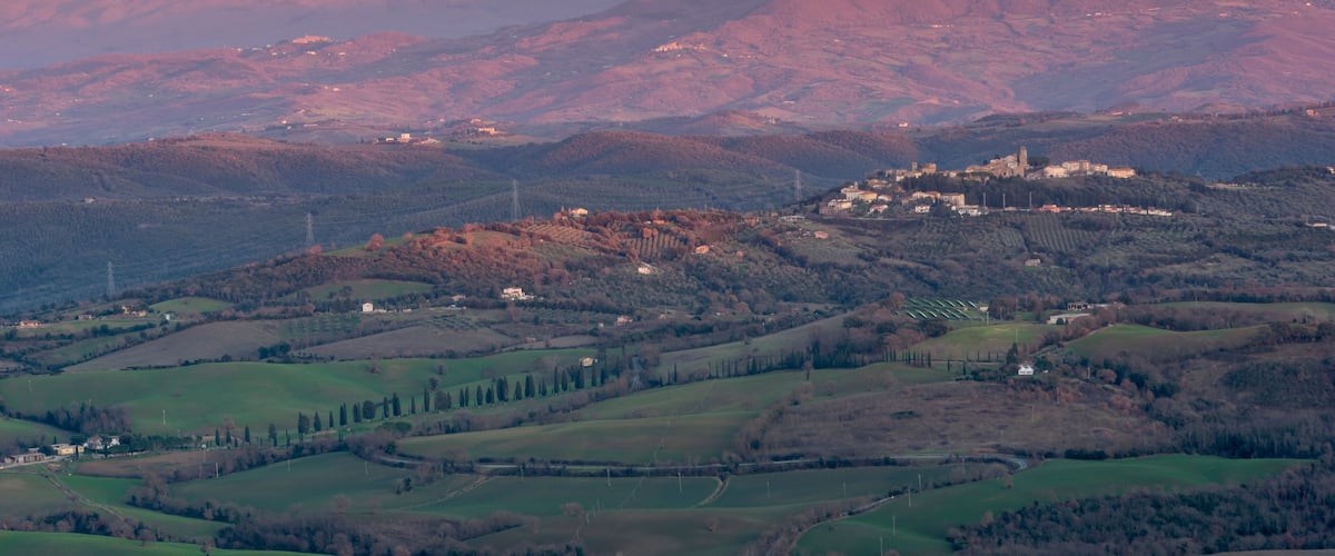 A mountainous landscape with a historic town on a hill, surrounded by fields and trees.