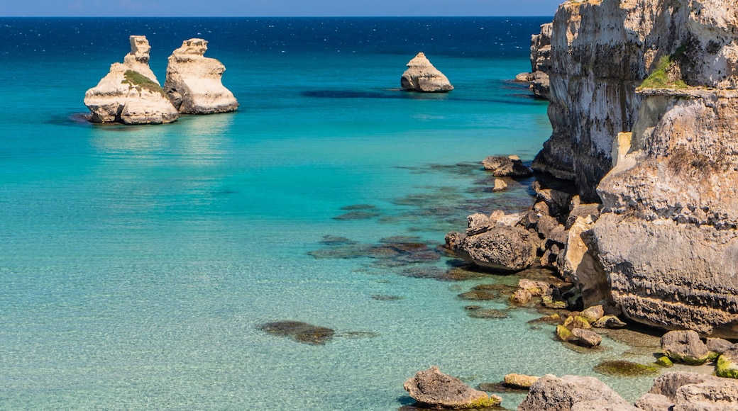 A coastal landscape with clear turquoise waters, rocky formations, and a sandy beach.