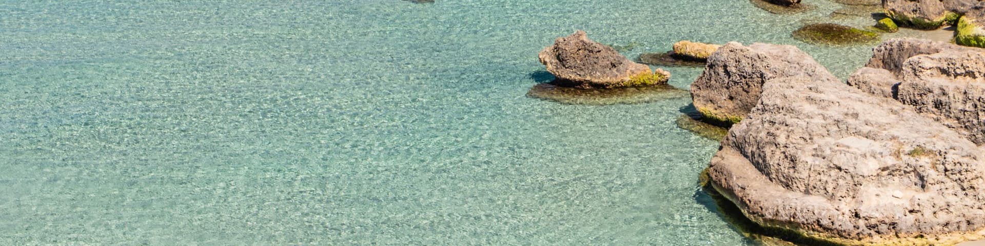 A coastal landscape with clear turquoise waters, rocky formations, and a sandy beach.