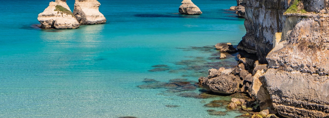 Un paisaje costero con aguas turquesas cristalinas, formaciones rocosas y una playa de arena.
