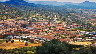 Un pueblo con edificios de techo rojo, una iglesia destacada y montañas al fondo.