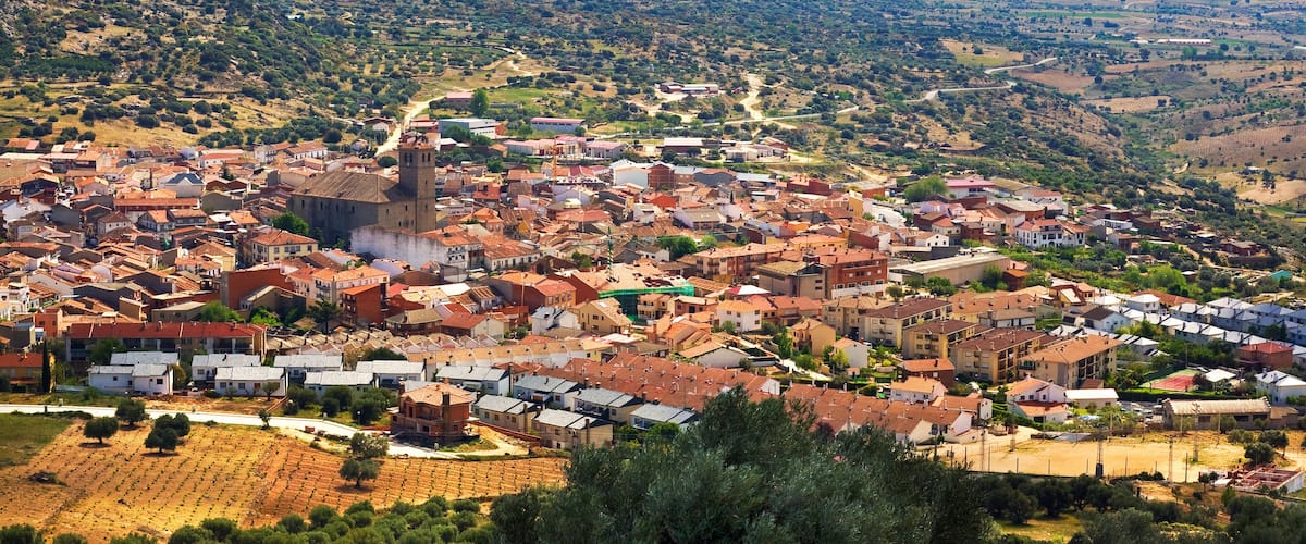 A town with red-roofed buildings, a prominent church, and mountains in the background.
