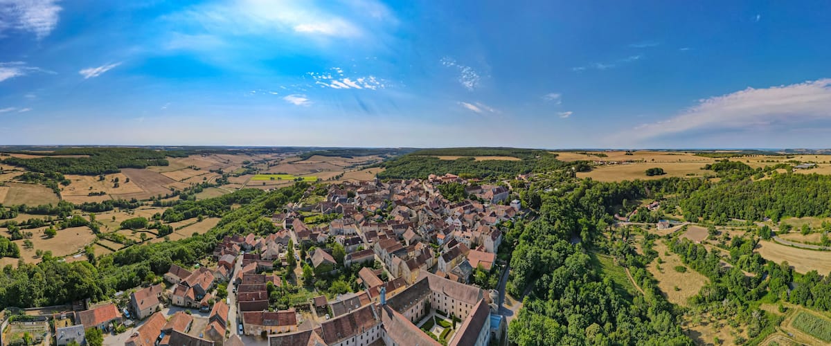 A panoramic view of a historic town with dense clusters of buildings, surrounded by lush green fields and rolling hills.