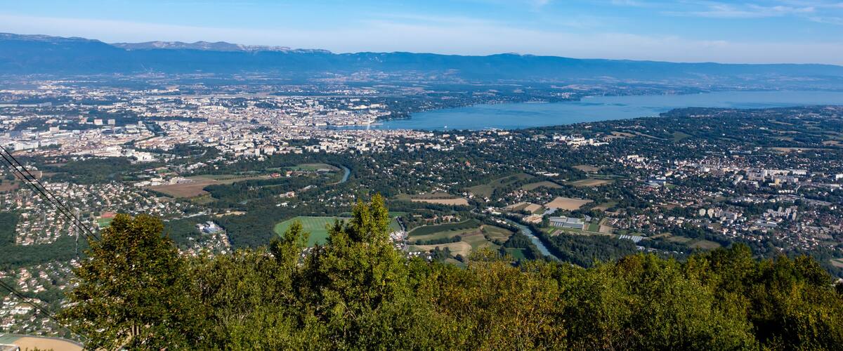 A panoramic view of a city with a river, surrounded by mountains and greenery.