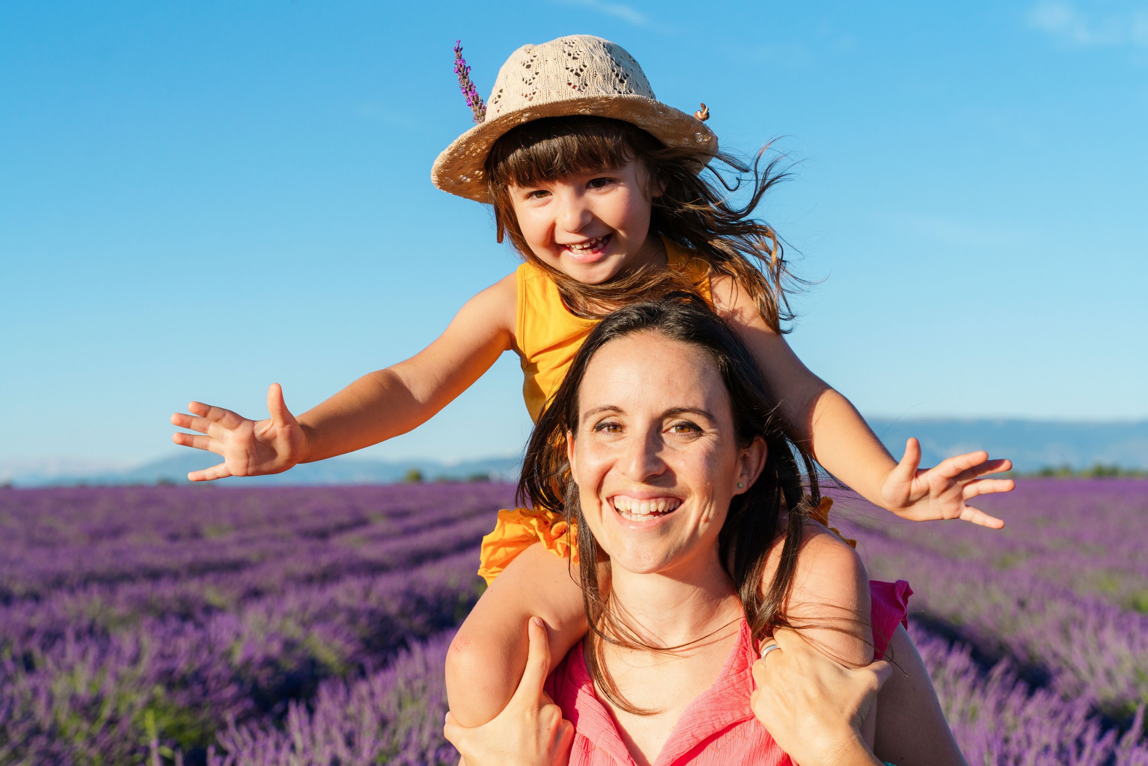 Portrait of mother piggybacking little daughter in vast summer lavender field