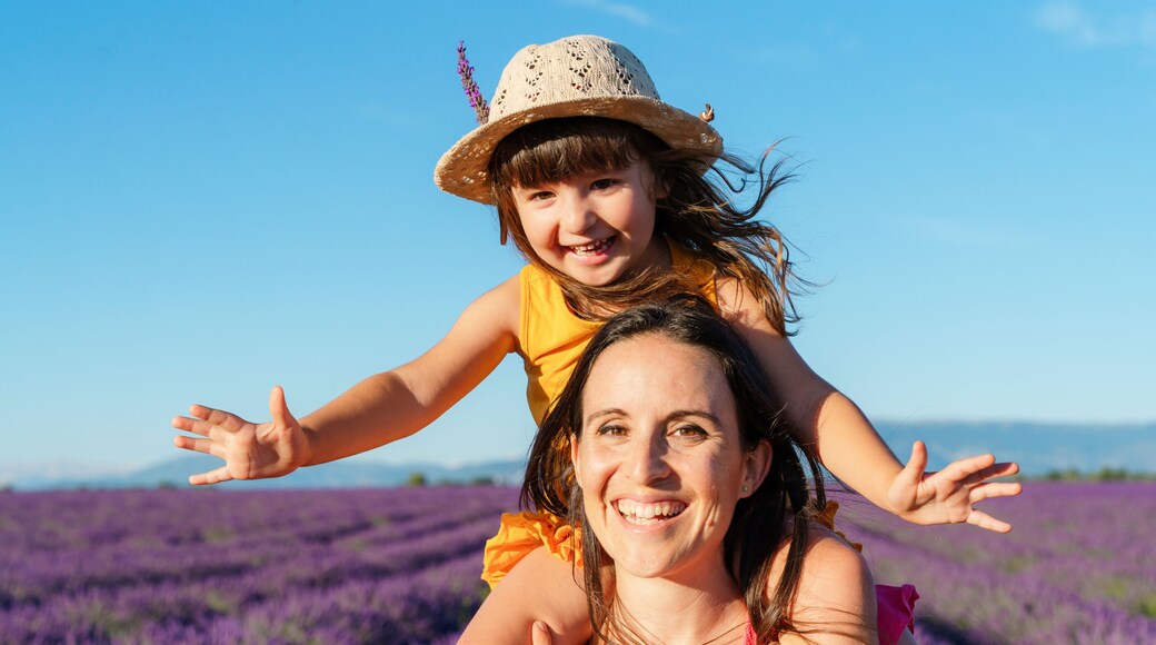 Portrait of mother piggybacking little daughter in vast summer lavender field