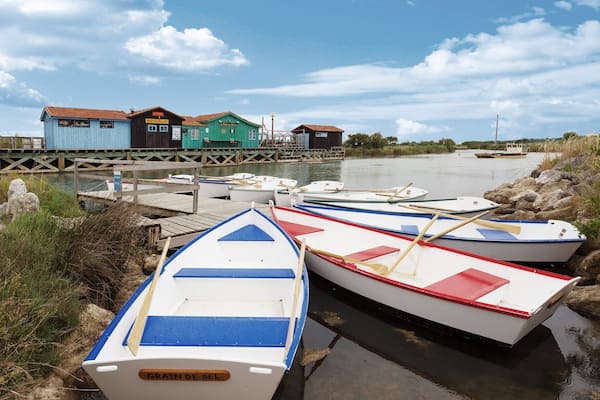 Un quai où sont amarrés plusieurs petits bateaux, une jetée en bois et des bâtiments portant des enseignes comme « Restaurant » et « Hôtel ».