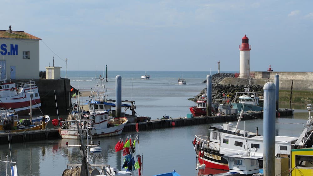 Un port avec des bateaux, un phare et un bâtiment sur lequel on peut lire « S.M. ».