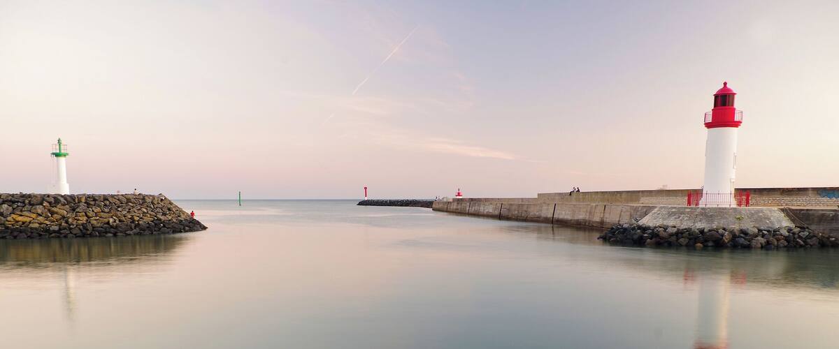 A calm harbor with two lighthouses, one green and white, the other red and white, and a stone breakwater.