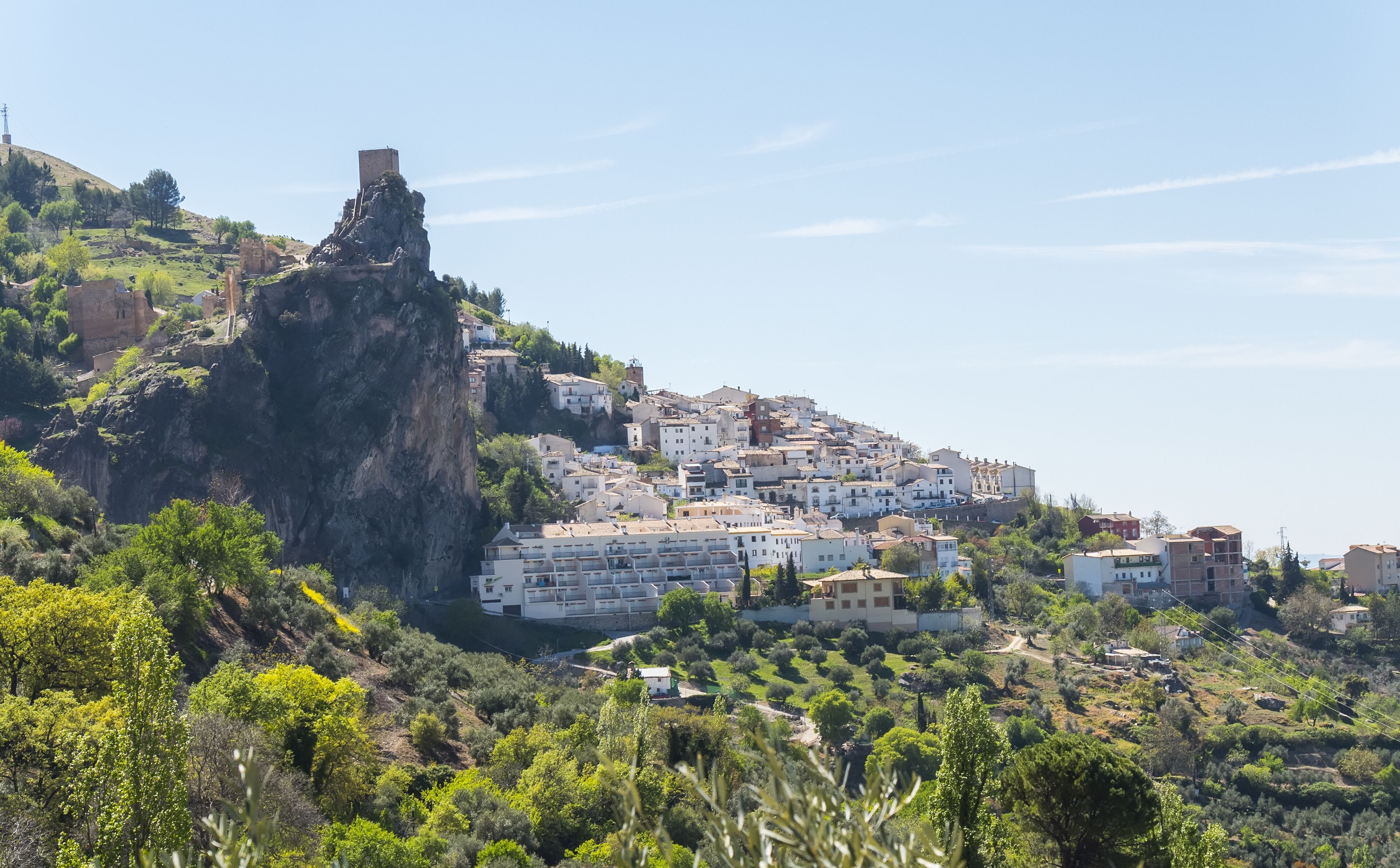 A coastal town with buildings on a hillside, a prominent rock formation, and lush greenery.