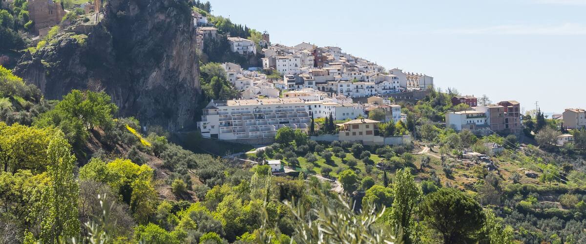 A coastal town with buildings on a hillside, a prominent rock formation, and lush greenery.