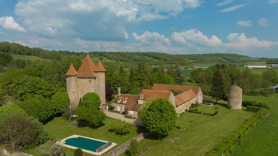 A castle with a tower, surrounded by lush green fields and a swimming pool.