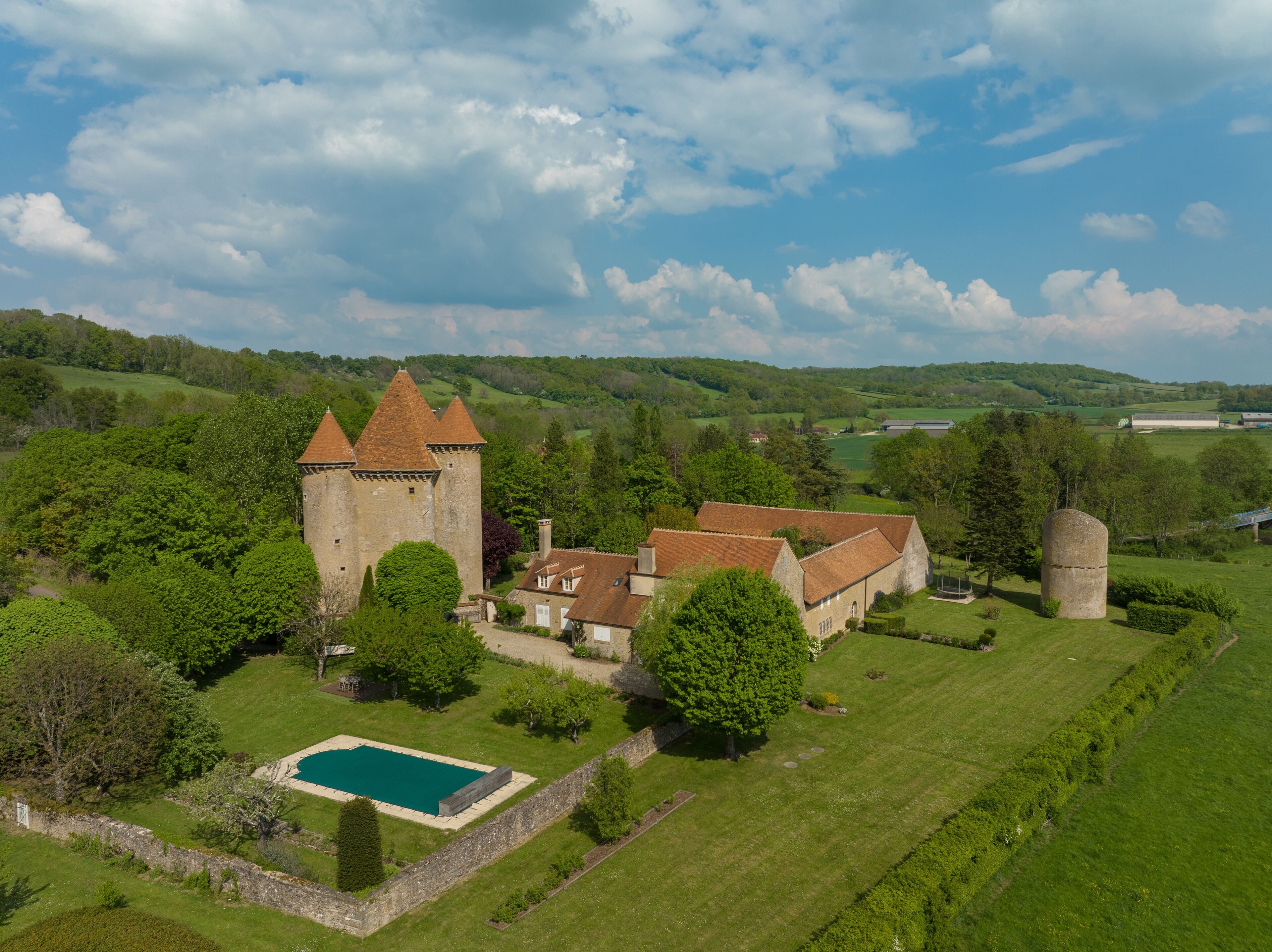 A castle with a tower, surrounded by lush green fields and a swimming pool.