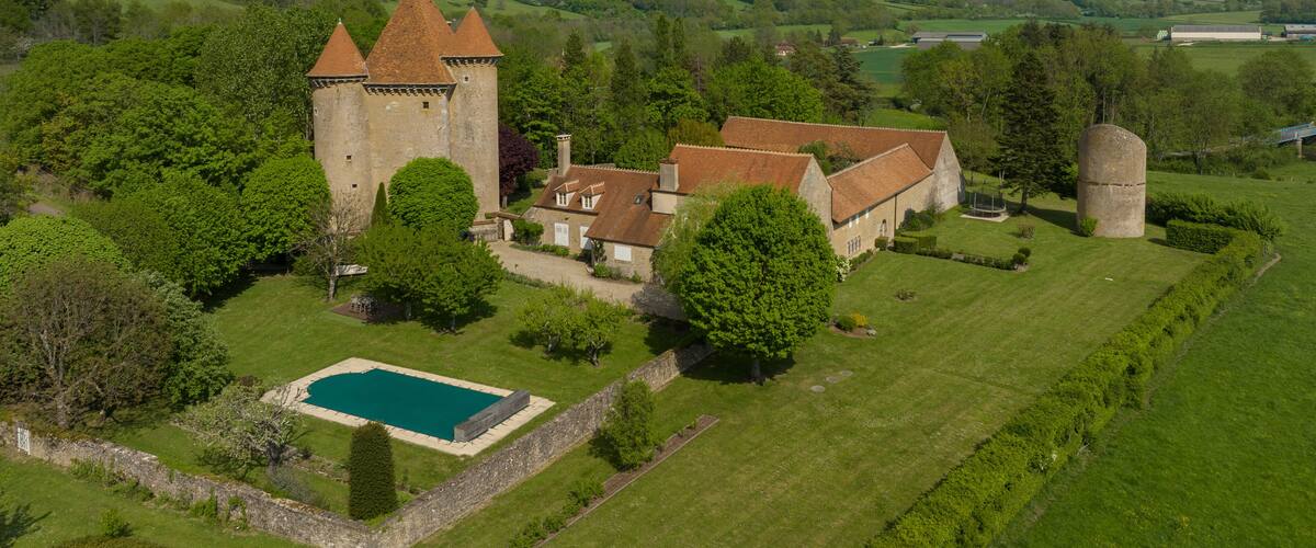 A castle with a tower, surrounded by lush green fields and a swimming pool.