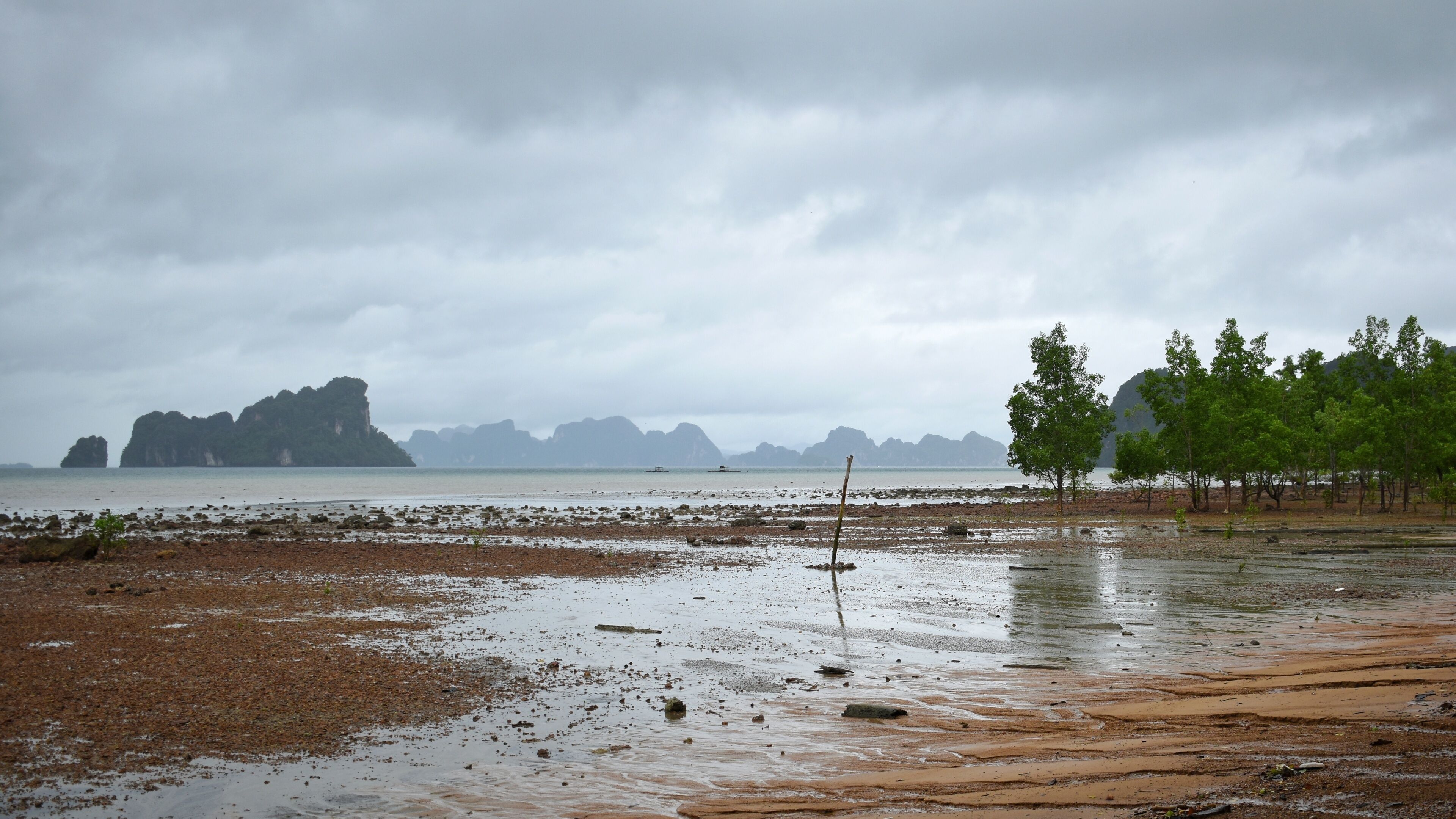 A coastal landscape with rocky shorelines, a small boat, and distant islands under a cloudy sky.