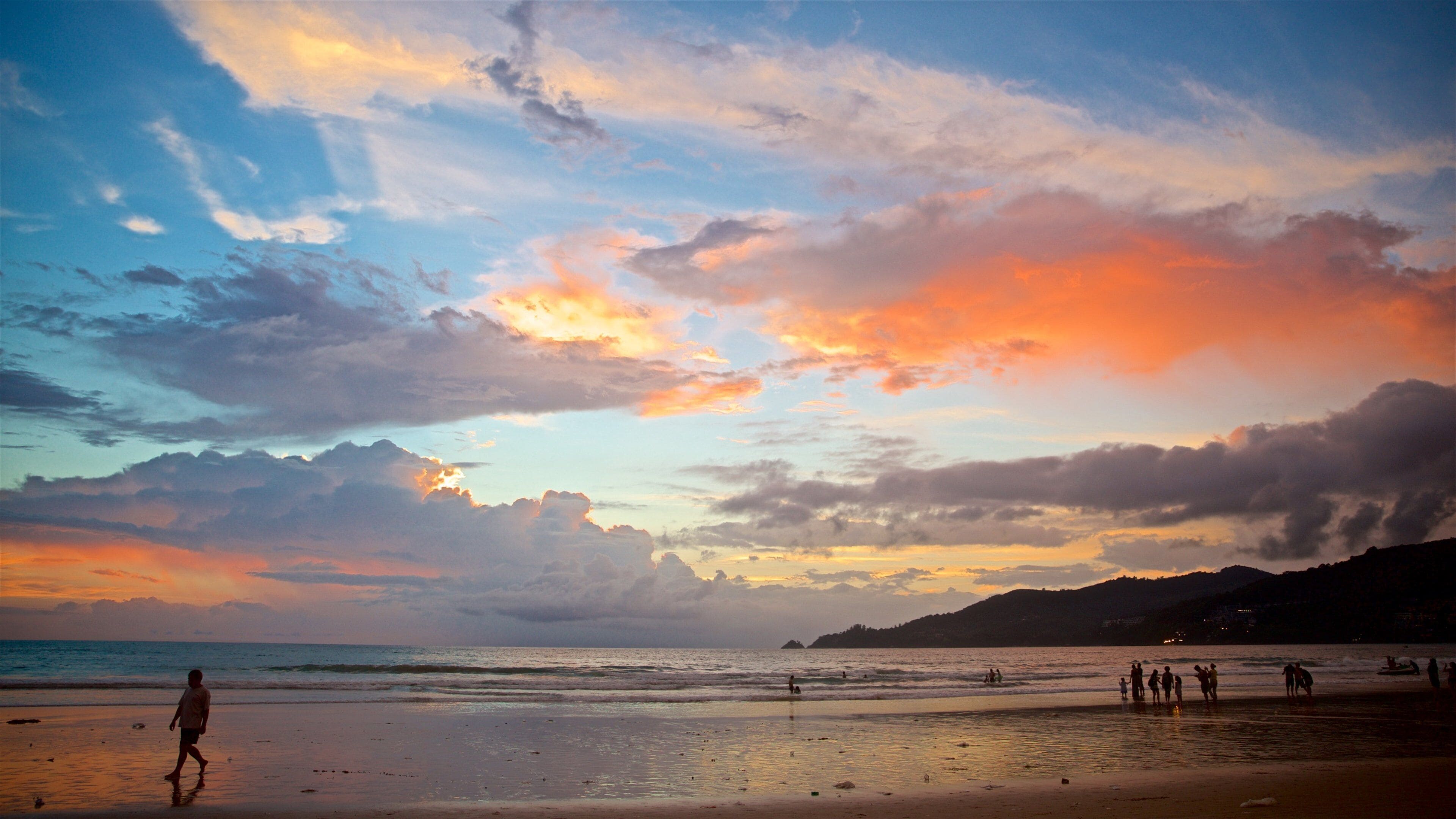 A beach at sunset with people walking and playing in the water.