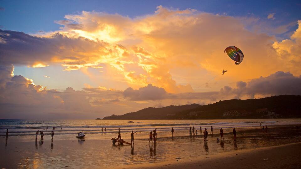 A beach with people, a kite surfer, and a sunset.