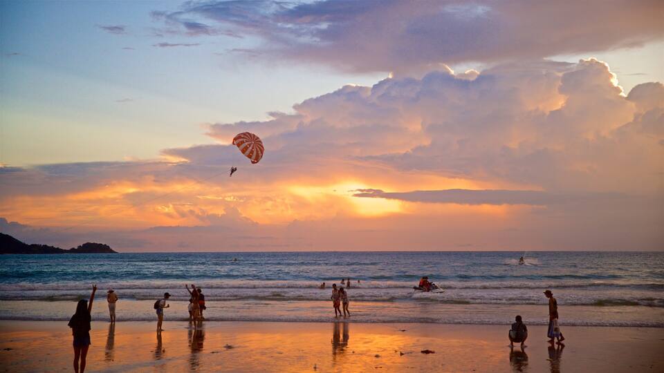 A beach at sunset with people, a parasail, and a sunset over the ocean.