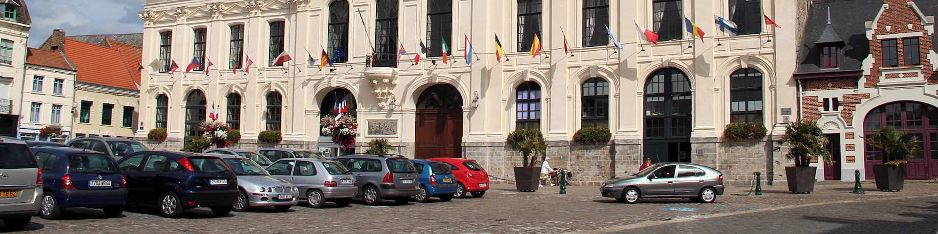 A historic building with ornate architecture, a prominent clock tower, and multiple flags.