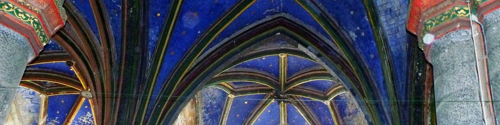 A Gothic-style ceiling with blue and green stained glass, arched columns, and intricate patterns.