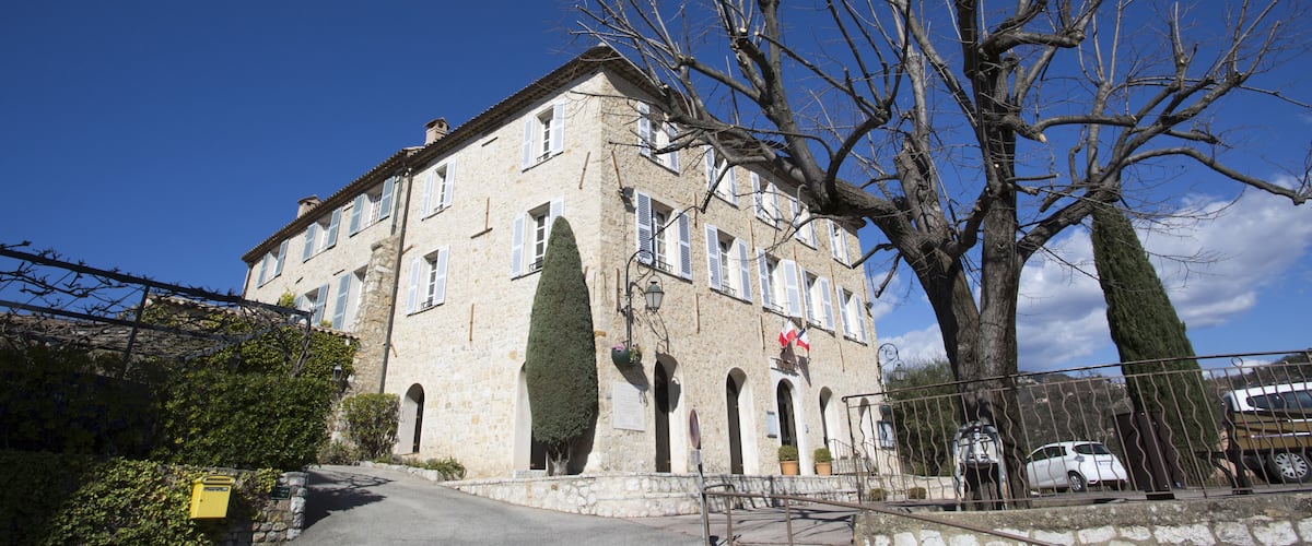 A stone building with arched windows and a large tree in front.