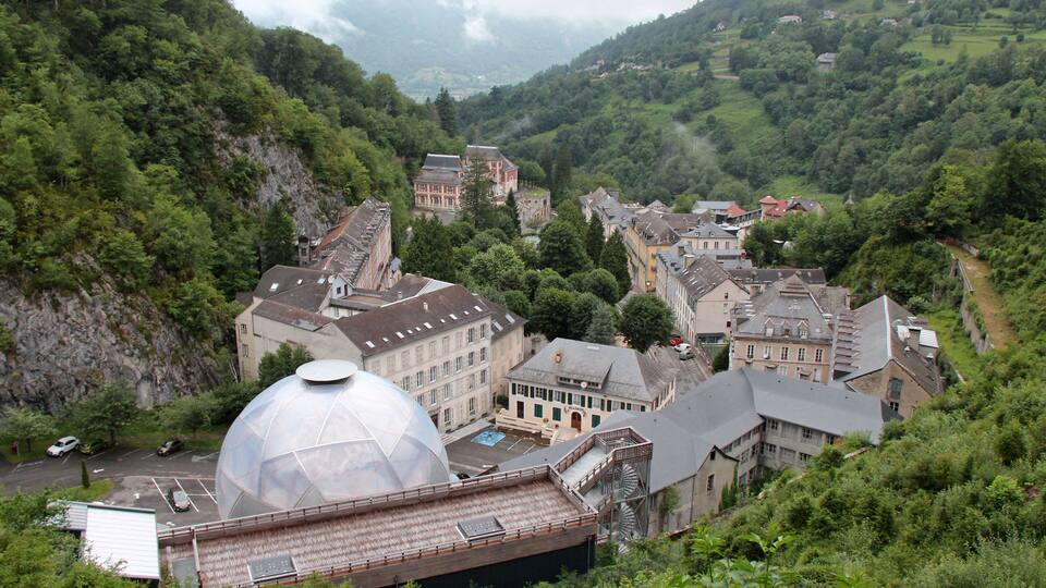 A town nestled in a valley with a prominent dome-shaped building, surrounded by lush greenery and traditional architecture.